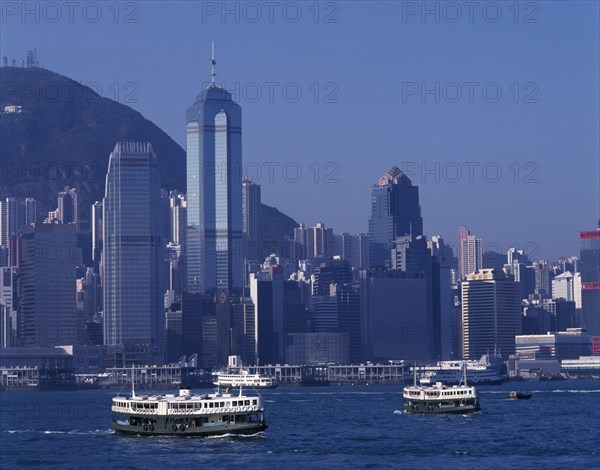 CHINA, Hong Kong, Victoria Harbour, Star Ferries crossing Victoria Harbour with high rise buildings on city skyline beyond.