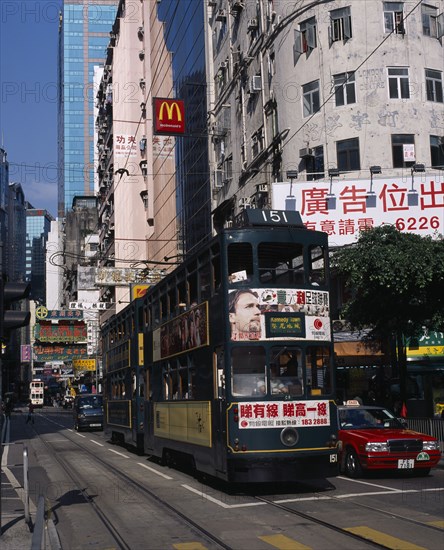 CHINA, Hong Kong, Hong kong Island tram on busy city street with high rise buildings and advertising hoardings.  Sign for McDonalds above tramline.