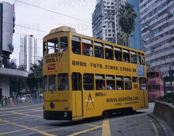 CHINA, Hong Kong, "Hong kong Island tram with passengers on top deck looking out of windows, advertising printed along the side and high rise buildings behind.  "