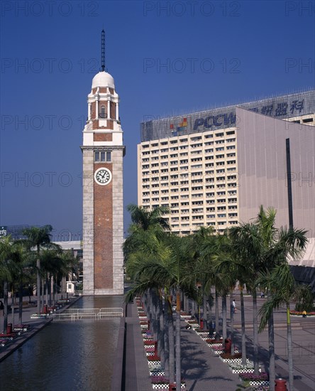CHINA, Hong Kong, Kowloon, Kowloon Star ferry clock tower at end of rectangular pool lined by palms and flowerbeds.
