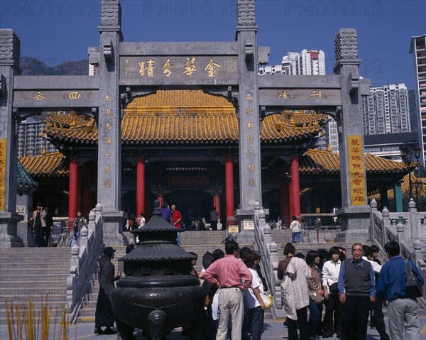 CHINA, Hong Kong, Kowloon, Wong Tai Sin taoist temple established in 1921.  Visitors beside incense burner at foot of flight of steps to entrance built in traditional Chinese style with red interior pillars and pagoda style roof.