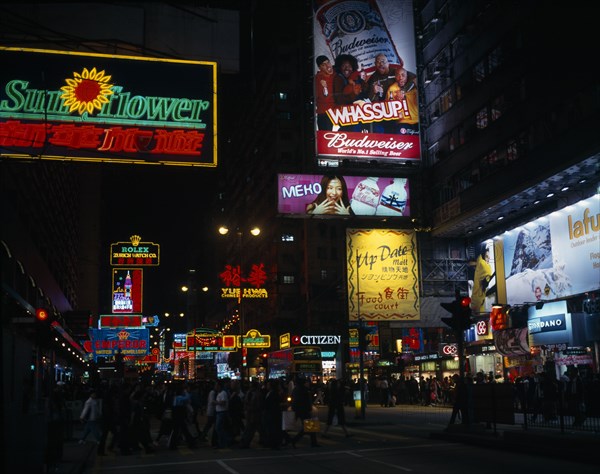 CHINA, Hong Kong, Kowloon, Illuminated advertising hoarding and neon signs on Nathan Road at night with crowds crossing road at traffic lights in foreground.