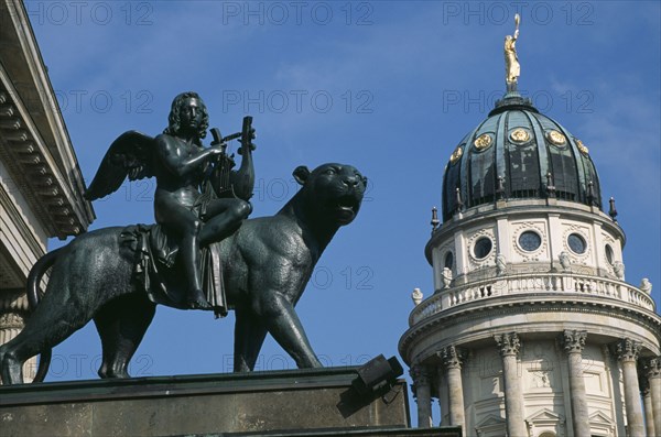 GERMANY, Berlin, Gendarmenmarkt.  Bronze statue of winged  lute playing Bacchus riding a panther in front of the Schauspielhaus with domed roof of the Franzosischer Dom behind.