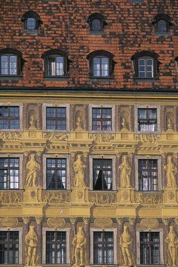 POLAND, Wroclaw, Detail of building facade with tromp l oeil painted mural creating effect of statuary and carved stonework.  Red tiled roof and multiple windows.