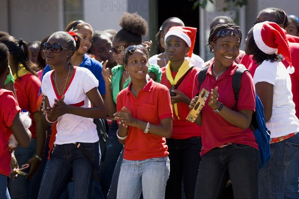 WEST INDIES, Grenada, St Georges, Girl Guides at Christmas singing carols in the street as part of their community service with one girl playing a tambourine