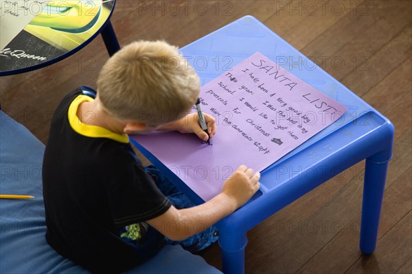 RELIGION, Festivals, Christmas, Young left handed boy at Christmas Eve sitting down and writing his Santa List at a table