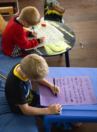 RELIGION, Festivals, Christmas, Two young left handed boys on Christmas Eve sitting down and writing their Santa Lists at tables