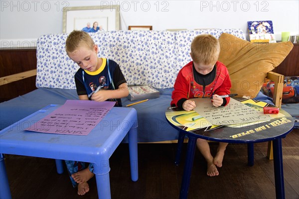 RELIGION, Festivals, Christmas, Two young left handed boys on Christmas Eve sitting down on a sofa and writing their Santa Lists at tables