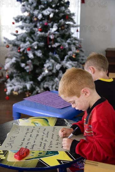 RELIGION, Festivals, Christmas, Two young left handed boys on Christmas Eve sitting down on a sofa and writing their Santa Lists at tables in front of the Christmas Tree