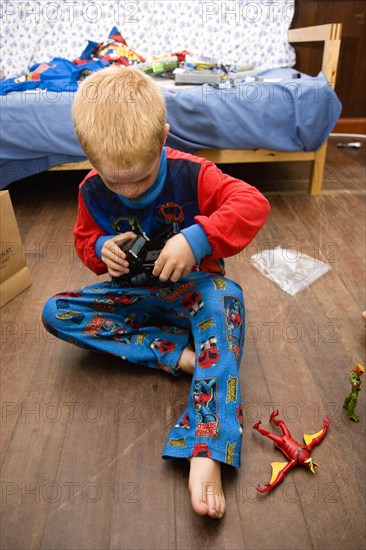 RELIGION, Festivals, Christmas, Young red headed boy in his pyjamas playing on the floor with his presents on Christmas Day