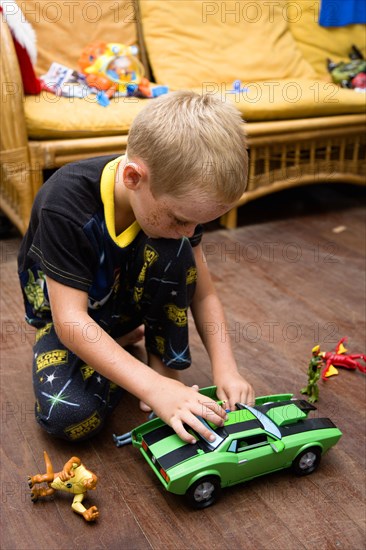 RELIGION, Festivals, Christmas, Young boy in his pyjamas playing on the floor with his green toy car and other presents on Christmas Day