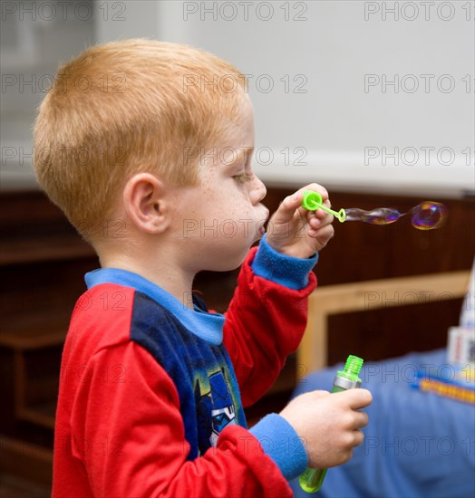 RELIGION, Festivals, Christmas, Young red headed boy in his pyjamas blowing soapy bubbles indoors