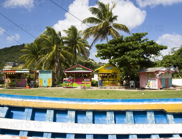 WEST INDIES, St Vincent And The Grenadines, Union Island, Colourful fruit and vegetable market stalls in Mulzac Square with a fishing boat in the foreground