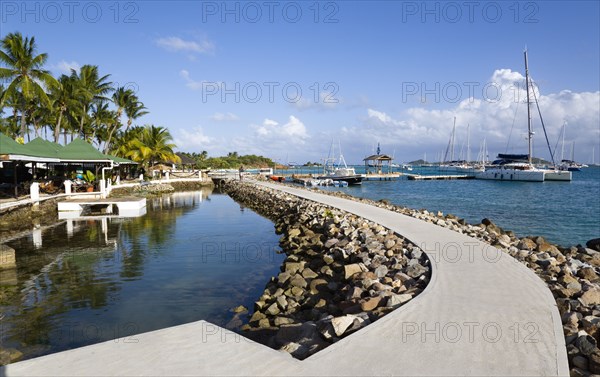 WEST INDIES, St Vincent And The Grenadines, Union Island, The concrete path around the shark pool at the Anchorage Yacht Club with boats moored in Clifton Harbour beyond