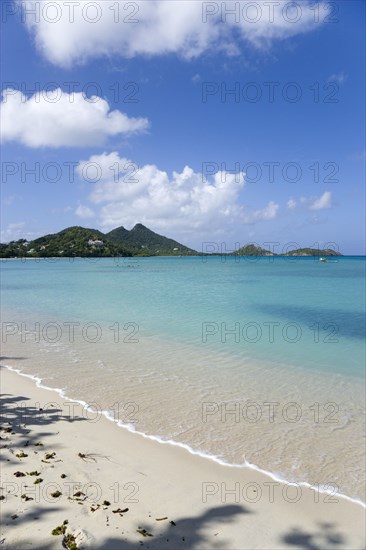 WEST INDIES, Grenada, Carriacou, The calm clear blue water breaking on Paradise Beach in L'Esterre Bay with Point Cistern and The Sister Rocks in the distance