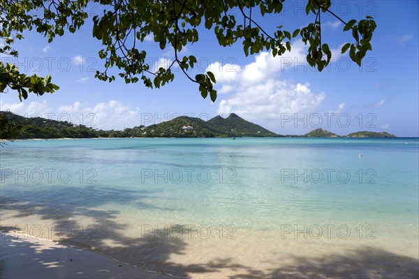 WEST INDIES, Grenada, Carriacou, The calm clear blue water breaking on Paradise Beach in L'Esterre Bay with Point Cistern and The Sister Rocks in the distance