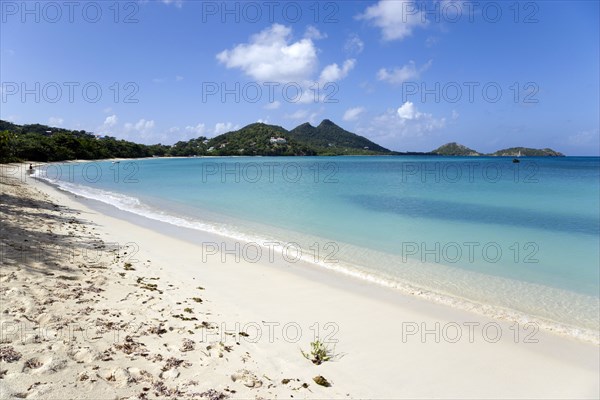 WEST INDIES, Grenada, Carriacou, Single person at the waters edge of the calm clear blue water breaking on Paradise Beach in L'Esterre Bay with Point Cistern and The Sister Rocks in the distance