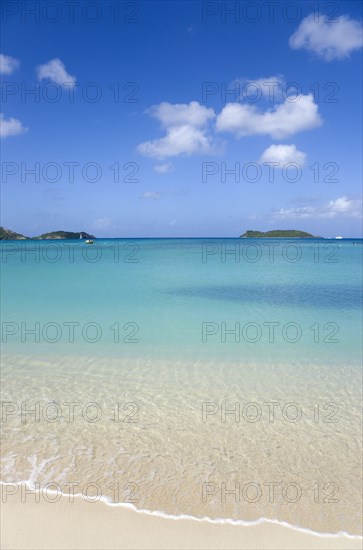 WEST INDIES, Grenada, Carriacou, The calm clear blue water breaking on Paradise Beach in L'Esterre Bay with The Sister Rocks and Mabouya Island in the distance