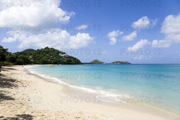 WEST INDIES, Grenada, Carriacou, The calm clear blue water breaking on Paradise Beach in L'Esterre Bay with Point Cistern and The Sister Rocks in the distance