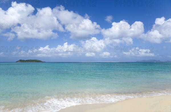 WEST INDIES, Grenada, Carriacou, The calm clear blue water breaking on Paradise Beach in L'Esterre Bay with Mabouya Island and Sandy Island in the distance