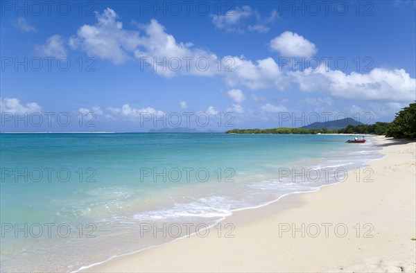 WEST INDIES, Grenada, Carriacou, The calm clear blue water breaking on Paradise Beach in L'Esterre Bay as two fishermen beach their boat with Sandy Island and Petite Martinique in the distance
