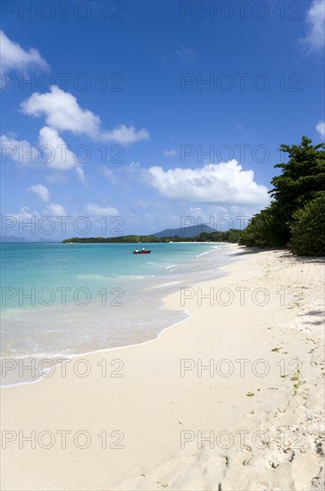 WEST INDIES, Grenada, Carriacou, The calm clear blue water breaking on Paradise Beach in L'Esterre Bay as two men beach their boat