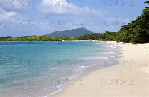 WEST INDIES, Grenada, Carriacou, The calm clear blue water breaking on Paradise Beach in L'Esterre Bay with High North mountain in the distance and people walking along the sandy shore