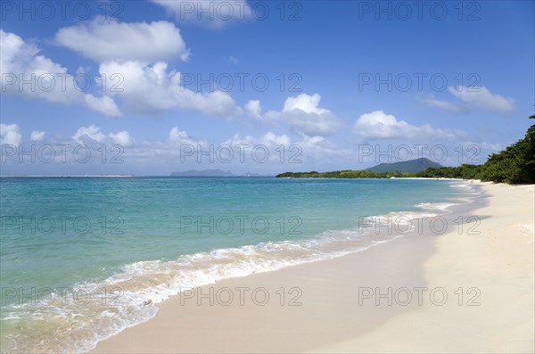 WEST INDIES, Grenada, Carriacou, "The calm clear blue water breaking on Paradise Beach in L'Esterre Bay with Sandy Island, Petite Martinique and High North mountain in the distance and people walking along the sandy shore"