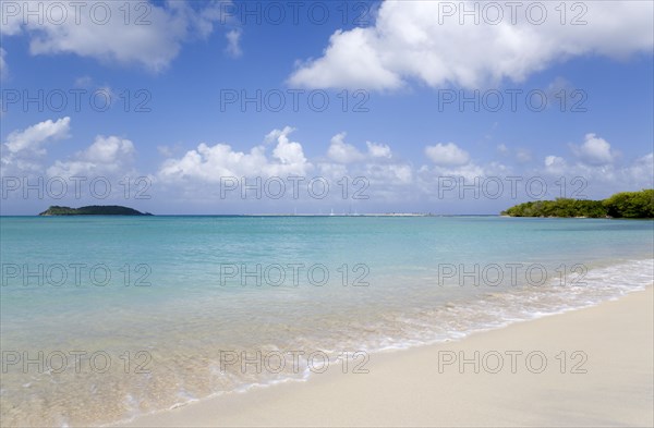 WEST INDIES, Grenada, Carriacou, The calm clear blue water breaking on Paradise Beach in L'Esterre Bay with Mabouya Island and Sandy Island in the distance