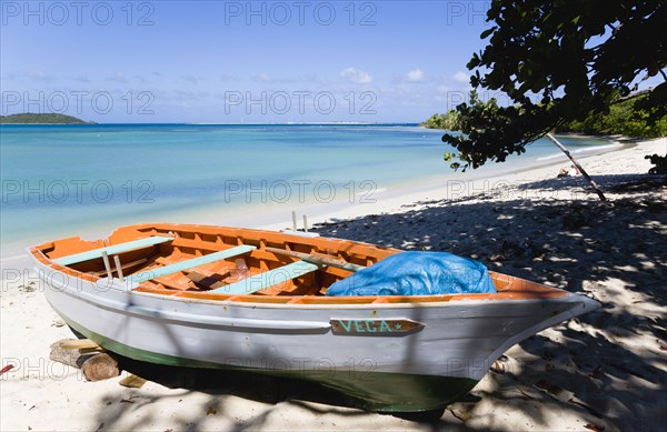 WEST INDIES, Grenada, Carriacou, The calm clear blue water breaking on Paradise Beach in L'Esterre Bay with Mabouya Island and Sandy Island in the distance. A small fishing boat sits on the beach out of the water