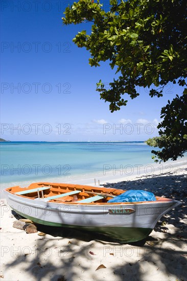 WEST INDIES, Grenada, Carriacou, The calm clear blue water breaking on Paradise Beach in L'Esterre Bay with Sandy Island in the distance. A small fishing boat sits on the beach out of the water