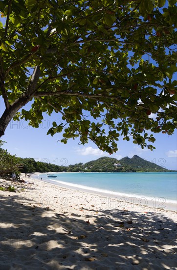 WEST INDIES, Grenada, Carriacou, The calm clear blue water breaking on Paradise Beach in L'Esterre Bay with Cistern Point in the distance. A small number of people on the beach and in the water