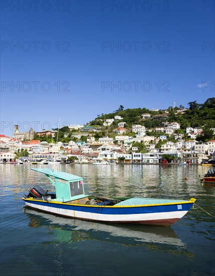 WEST INDIES, Grenada, St George, Fishing boat moored in the Carenage harbour of the capital city of St George's with houses and the roofless cathedral damaged in Hurricane Ivan on the nearby hill