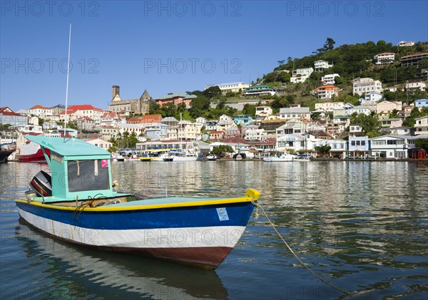 WEST INDIES, Grenada, St George, Fishing boat moored in the Carenage harbour of the capital city of St George's with houses and the roofless cathedral damaged in Hurricane Ivan on the nearby hill