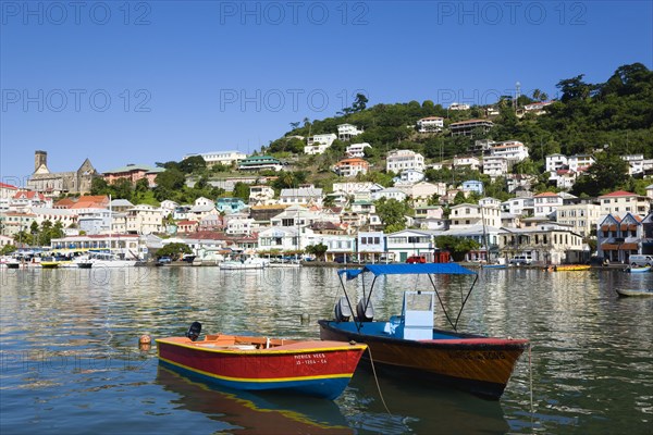WEST INDIES, Grenada, St George, Water taxi boats moored in the Carenage harbour of the capital city of St George's with houses and the roofless cathedral damaged in Hurricane Ivan on the nearby hill