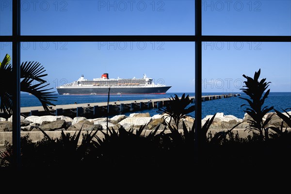WEST INDIES, Grenada, St George, The Queen Mary 2 liner at anchor beyond a jetty off the capital city of St George's seen through the window of the cruise ship terminal