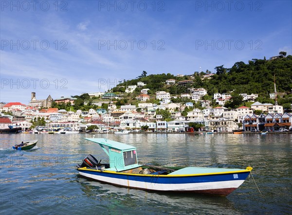 WEST INDIES, Grenada, St George, Fishing boat moored in the Carenage harbour of the capital city of St George's with houses and the roofless cathedral damaged in Hurricane Ivan on the nearby hill. A boy in a speedboat heads inshore past the fishing boat