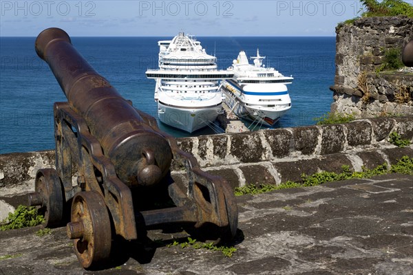 WEST INDIES, Grenada, St George, An old canon pointing out to sea at Fort George with two cruise ships the Caribbean Princess and the Aida Aura moored below at the cruise ship terminal in the capital city of St George's with passengers walking on the jetty between the two liners