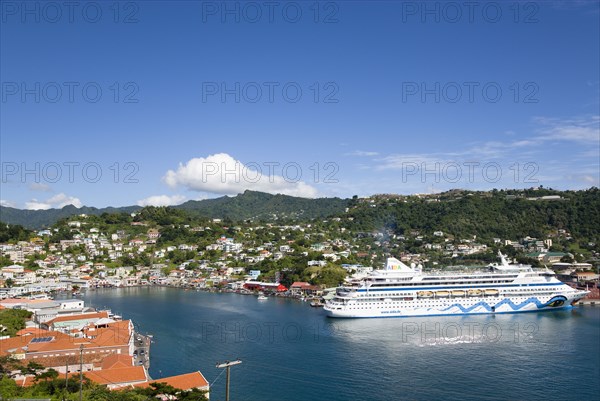 WEST INDIES, Grenada, St George, The Carenage harbour of the capital city of St George's surrounded by hills lined with houses and other buildings and the cruise ship Aida Aura moored at the docks