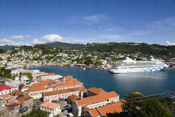 WEST INDIES, Grenada, St George, The Carenage harbour of the capital city of St George's surrounded by hills lined with houses and other buildings and the cruise ship Aida Aura moored at the docks