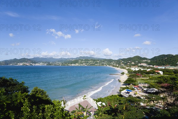 WEST INDIES, Grenada, St George, Waves of the aquamarine sea breaking on the two mile stretch of Grand Anse Beach with people on the white sandy beach and the capital city of St George's in the distance