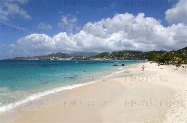 WEST INDIES, Grenada, St George, Waves of the aquamarine sea breaking on the two mile stretch of Grand Anse Beach with people on the white sandy beach and the capital city of St George's in the distance