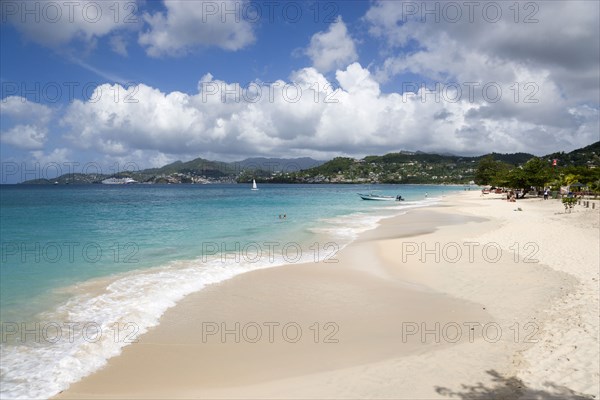 WEST INDIES, Grenada, St George, Waves of the aquamarine sea breaking on the two mile stretch of Grand Anse Beach with people on the white sandy beach and the capital city of St George's in the distance