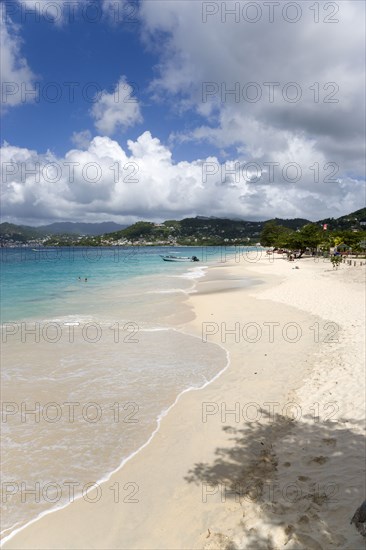 WEST INDIES, Grenada, St George, Waves of the aquamarine sea breaking on the two mile stretch of Grand Anse Beach with people on the white sandy beach and the capital city of St George's in the distance