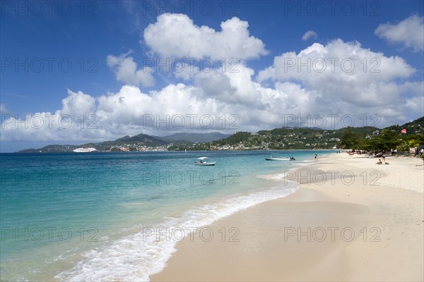 WEST INDIES, Grenada, St George, Waves of the aquamarine sea breaking on the two mile stretch of Grand Anse Beach with people on the white sandy beach and the capital city of St George's in the distance