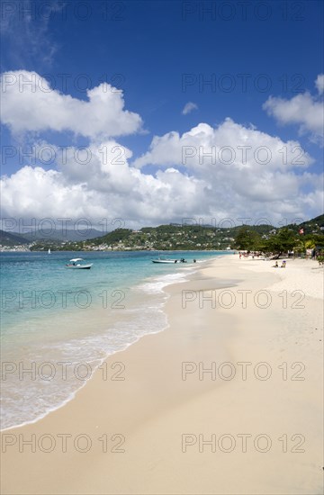 WEST INDIES, Grenada, St George, Waves of the aquamarine sea breaking on the two mile stretch of Grand Anse Beach with people on the white sandy beach and the capital city of St George's in the distance