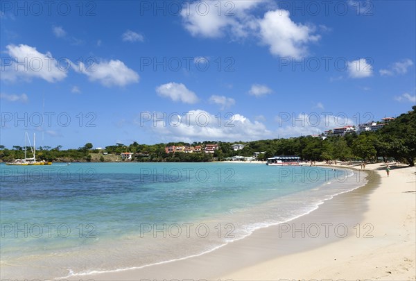 WEST INDIES, Grenada, St George, The aquamarine sea and tree lined white sand of BBC Beach in Morne Rouge Bay with tourists walking on the beach and tour boats moored