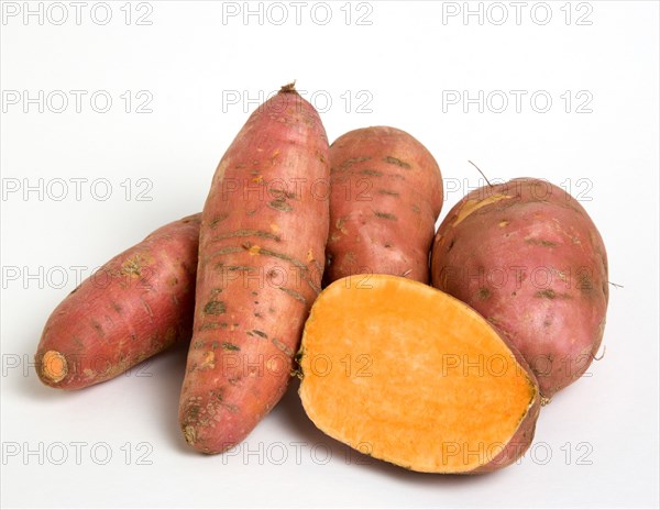 FOOD, Vegetable, Root Vegetable, Group shot of North American sweet potatoes on a white background with on potato cut in half showing the orange coloured centre