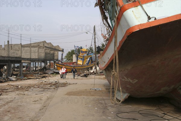 THAILAND, Phang Nga District, Nam Khem, "Tsunami. People walk past boats that have been pushed onto the streets in the village, nothing is left standing in the village 2500 people are pressumed dead 125kms north of Phuket on the 2nd Jan"