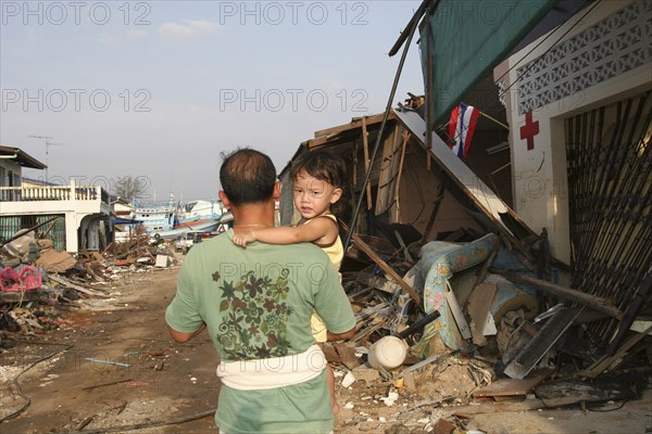 THAILAND, Phang Nga District, Nam Khem, Tsunami. One of the villagers with his child walks passed the remains of of his village after the damaged caused by the tsunami.Nothing is left standing in the village 2500 people are pressumed dead. 125kms north of Phuket on the 2nd Jan.